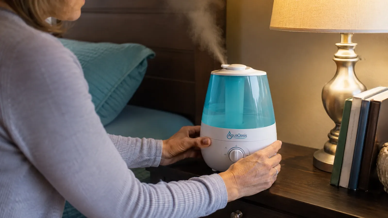 Hands setting an AquaOasis humidifier on a nightstand and adjusting the rotating mist nozzle