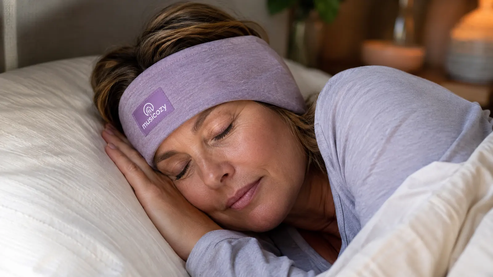 Close-up of a woman lying on her side with a stretchy headband over her ears, cheek resting on the pillow