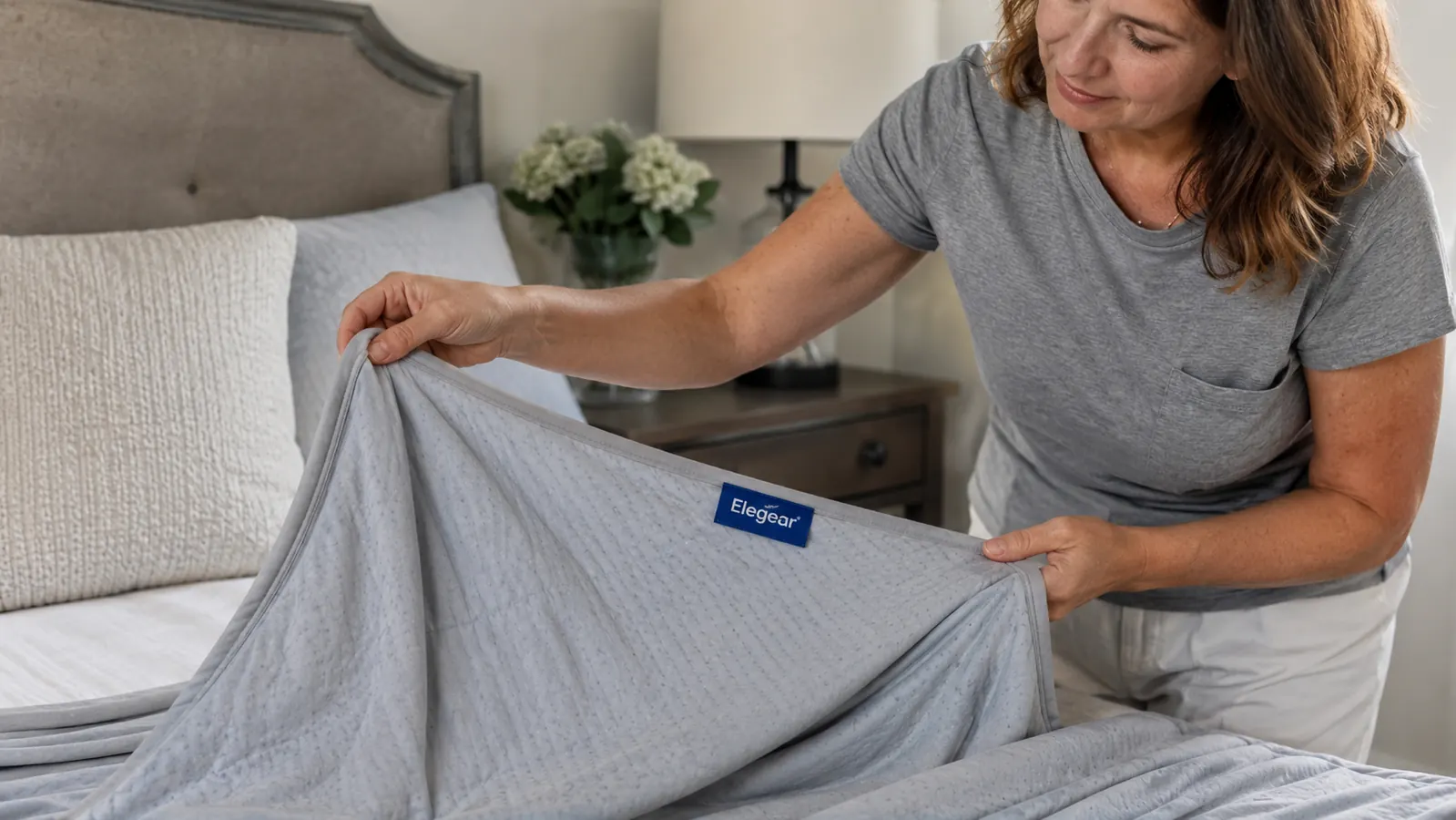 Close-up of a hand pulling back the corner of the Elegear cooling blanket to show its smooth, silky-looking fabric texture