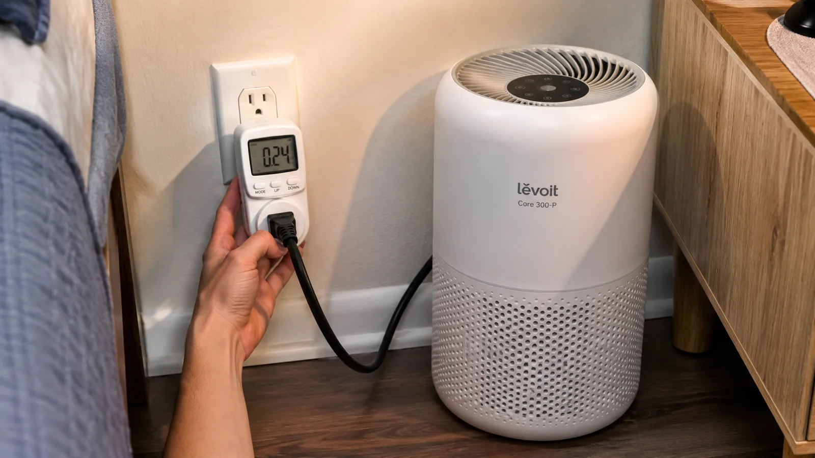 Hand holding a small plug-in wattage meter next to an air purifier's power cord