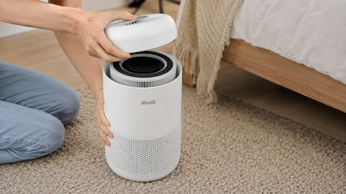 Close-up of a hand lifting the top panel off a white air purifier to show the filter underneath